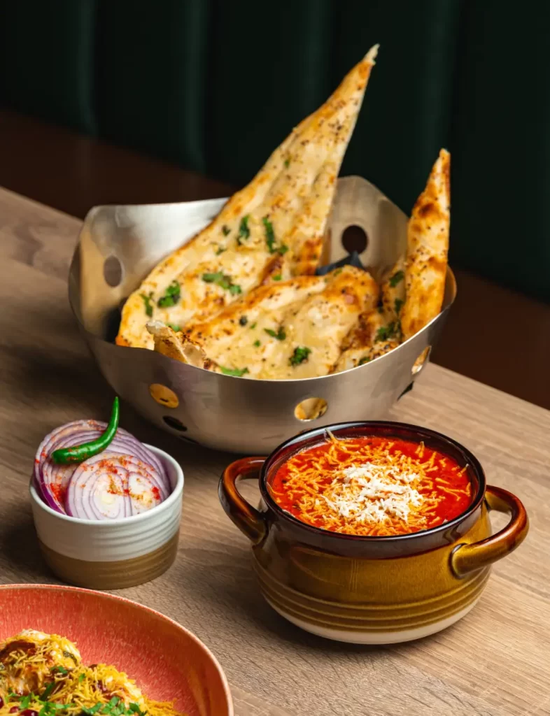 Indian meal featuring garlic naan, rich red curry, and fresh onions